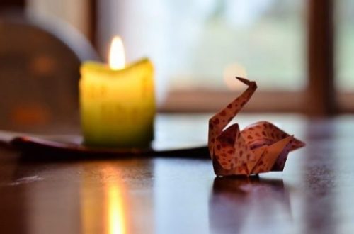Origami Swan Illuminated By Candle Light On Table.